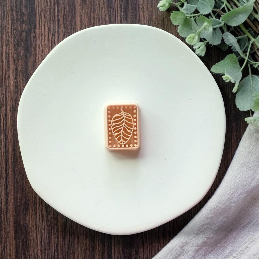 rectangle leaf polymer clay cutter on white plate with greenery and wood background