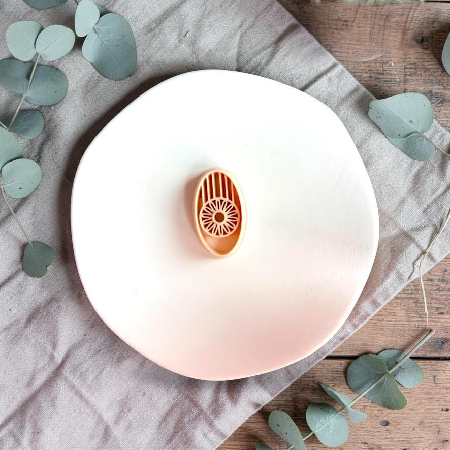 Oval sunburst polymer clay cutter on white plate with neutral fabric and greenery