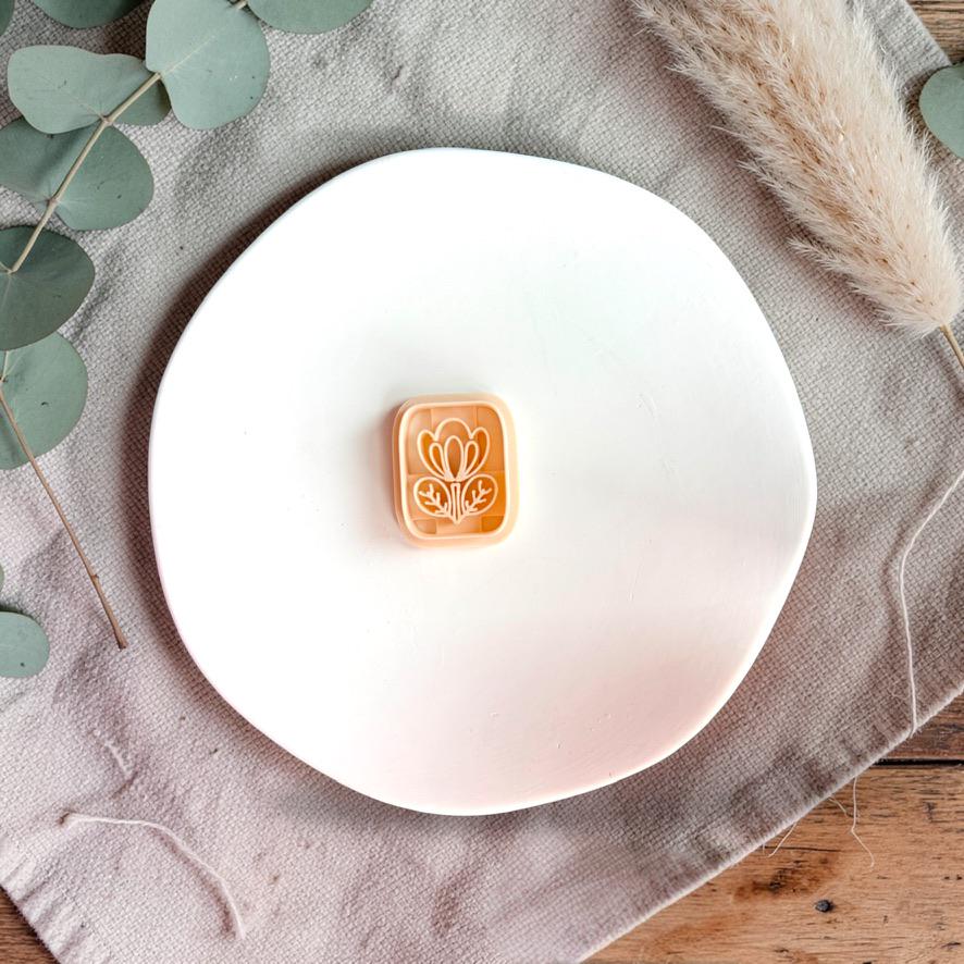 Floral tile polymer clay cutter on white plate with neutral fabric and greenery