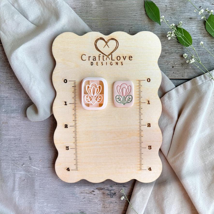 Floral tile cutter and finished clay piece displayed on wooden measurement board