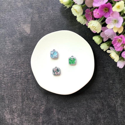Three mini square floral clay charms displayed on white surface