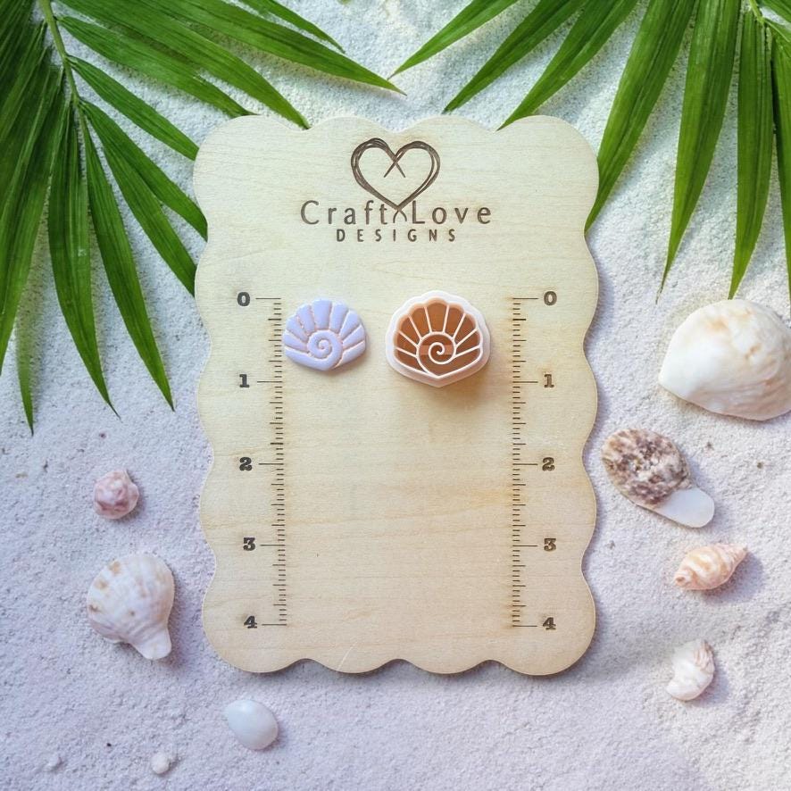 Spiral seashell cutter and clay sample displayed on wooden sizing board with shells and palm leaves