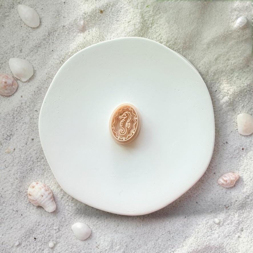 Seahorse polymer clay cutter shown on white plate with beach sand and shells