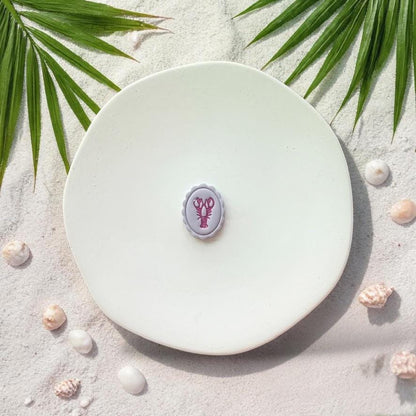 Finished lobster cameo clay piece on white plate with coastal sand and shells