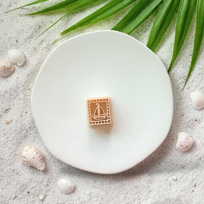 Sailboat clay cutter on white plate with sand, seashells, and tropical leaves