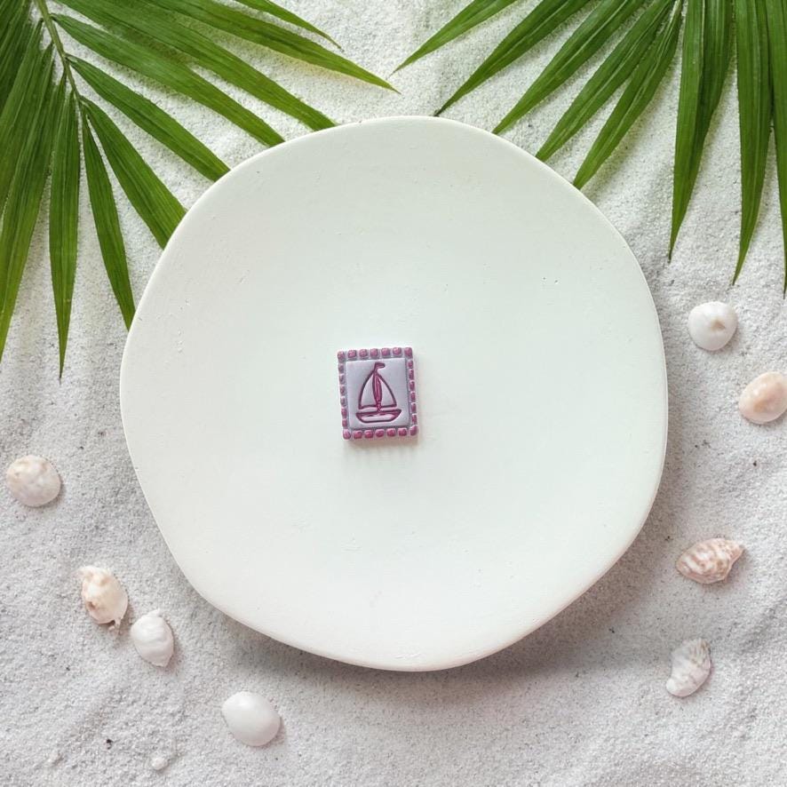 Finished sailboat clay piece on white plate with beach sand and shells