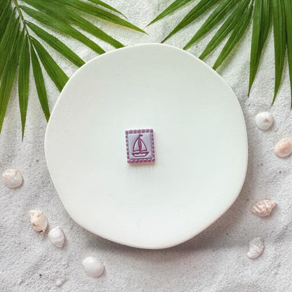 Finished sailboat clay piece on white plate with beach sand and shells