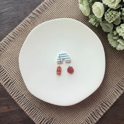 arch apple and pencil clay earrings on white plate with burlap cloth