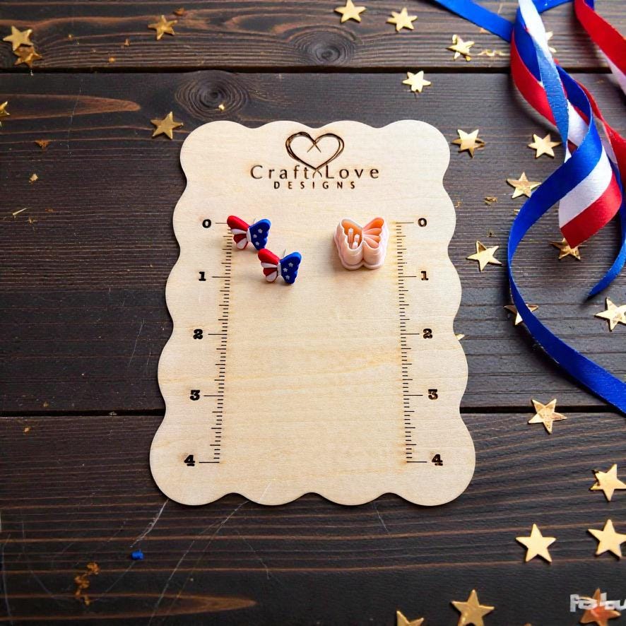 Patriotic butterfly clay earrings and matching cutter displayed on wooden measurement board with gold stars and ribbon