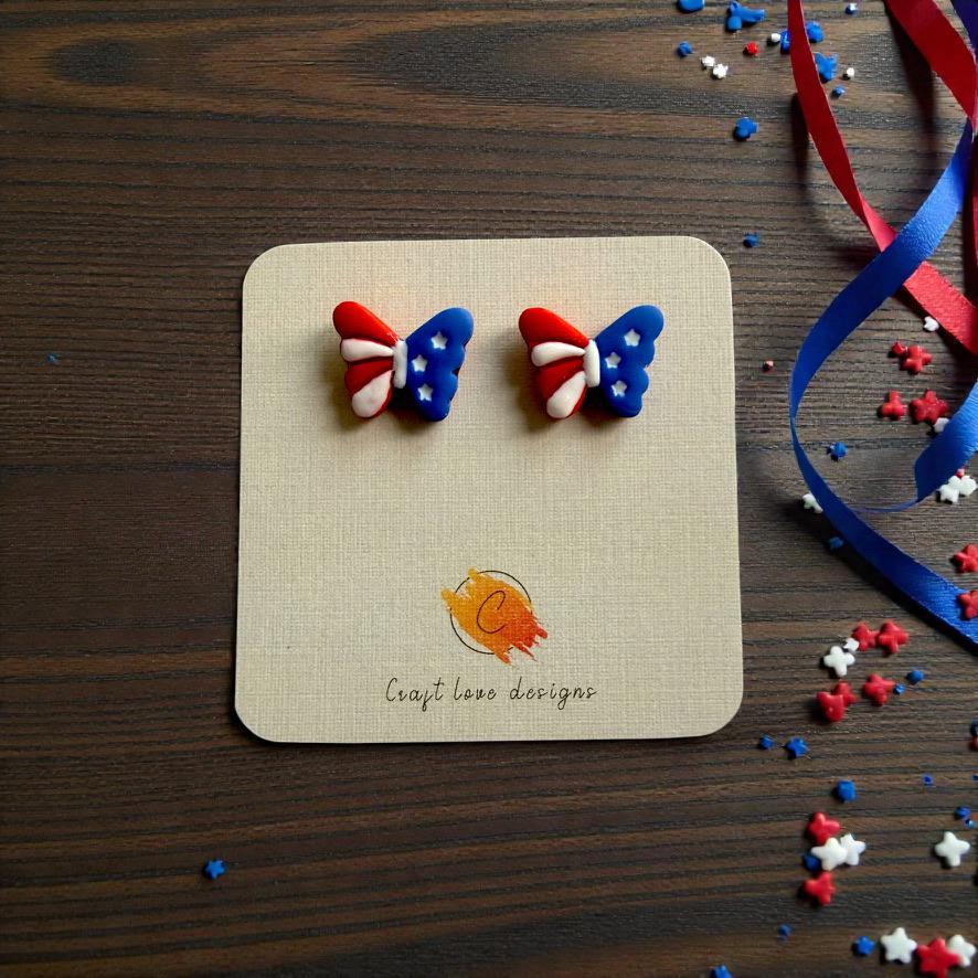 Pair of red white and blue butterfly clay earrings displayed on a card with patriotic curling ribbon decorations