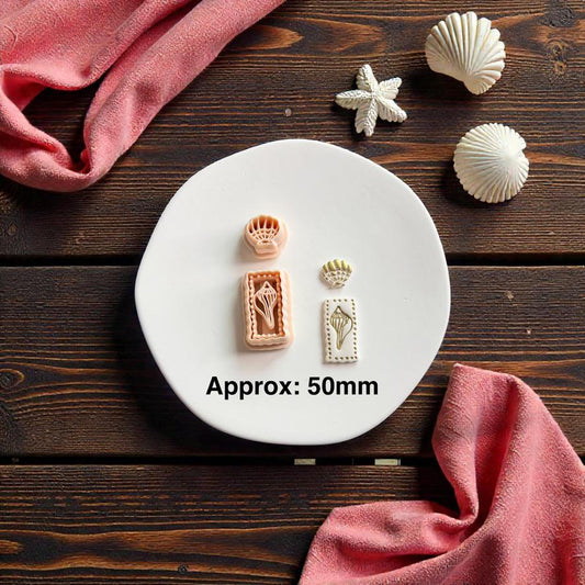 Seashell polymer clay cutter set displayed on white clay slab with beach themed seashell decorations and pink fabric