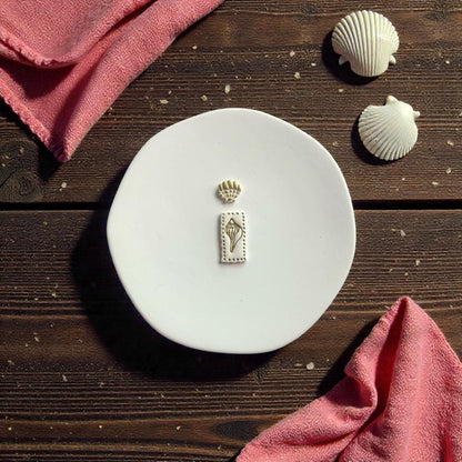 Coastal shell polymer clay earrings shown beside matching cutter on white ceramic surface with seashell props