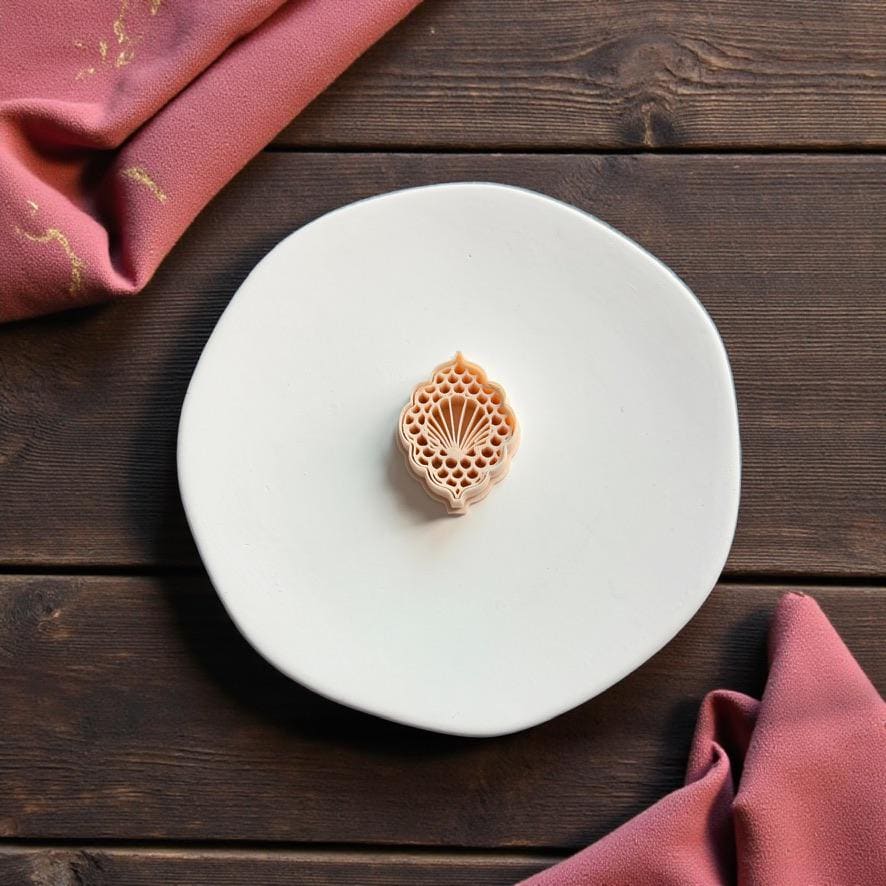 Ornate seashell polymer clay cutter displayed on white ceramic plate with coastal themed styling and pink fabric background