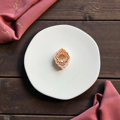 Ornate seashell polymer clay cutter displayed on white ceramic plate with coastal themed styling and pink fabric background