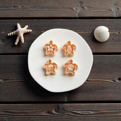 Four sea turtle polymer clay cutters with tropical center designs displayed on white ceramic plate with beach themed coastal decor