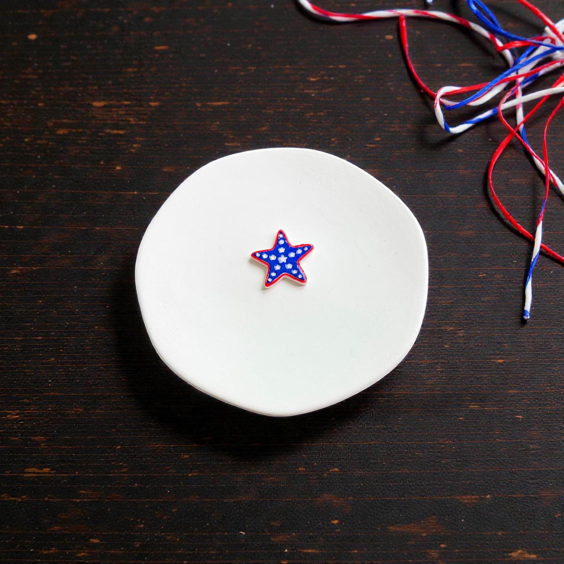 Finished patriotic starfish clay earring in red white and blue colors displayed on white ceramic plate with festive ribbon styling