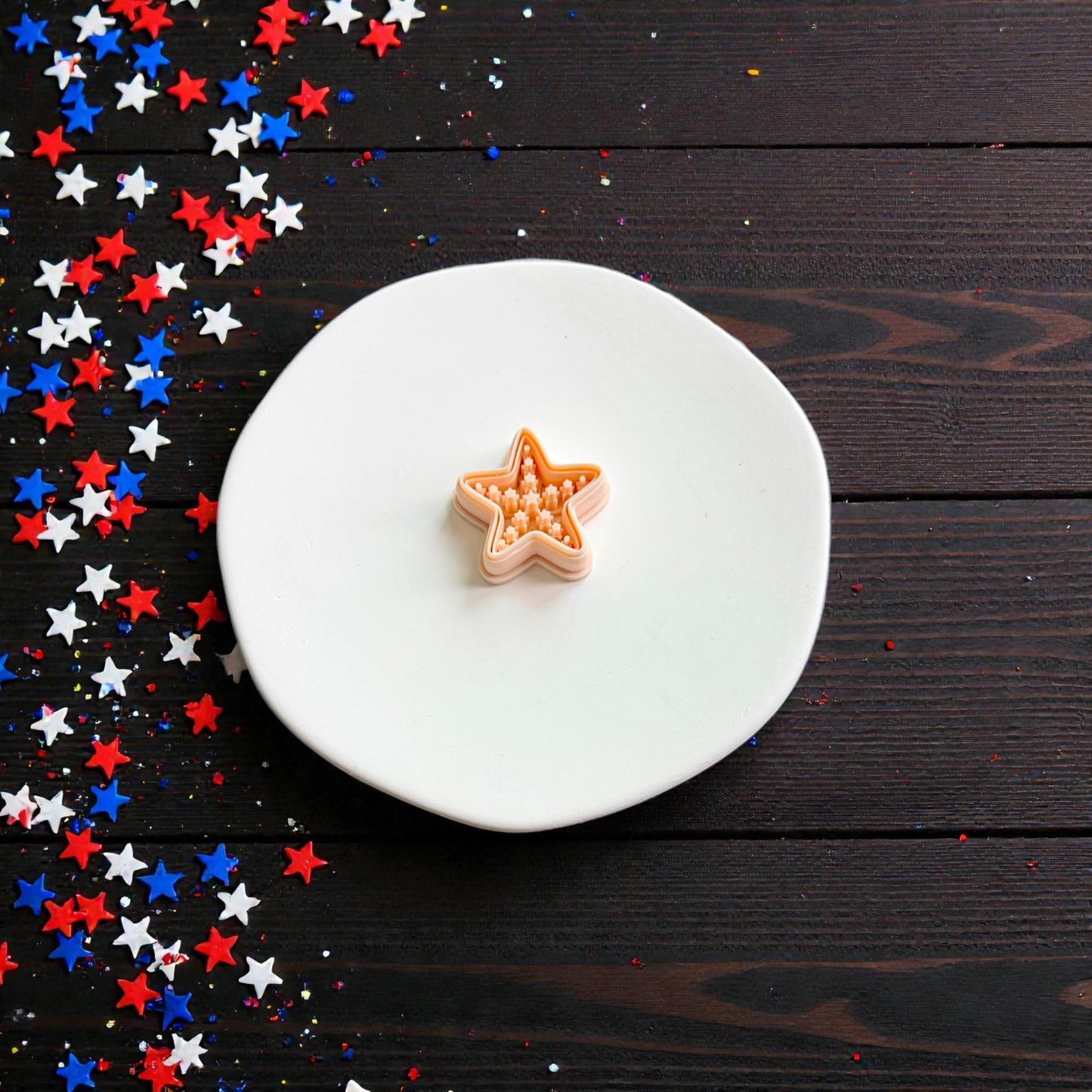 Americana starfish polymer clay cutter displayed on white ceramic plate with patriotic red white and blue star confetti