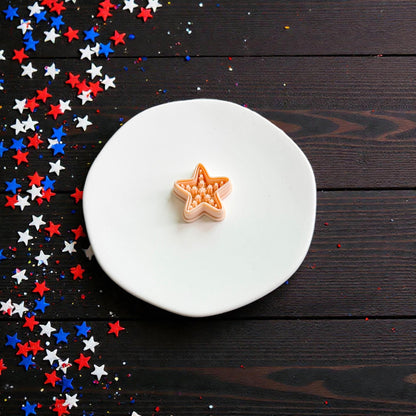 Americana starfish polymer clay cutter displayed on white ceramic plate with patriotic red white and blue star confetti