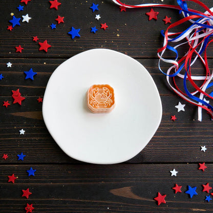 Patriotic crab polymer clay cutter displayed on white ceramic plate with red white and blue ribbon and star confetti for Fourth of July theme