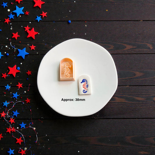 Patriotic seahorse polymer clay cutter with finished clay design displayed on white ceramic plate showing approximate 38mm size