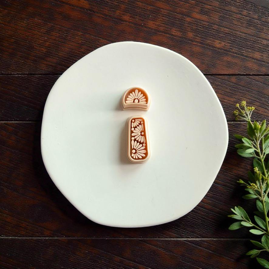 Daisy floral polymer clay cutter set displayed on white ceramic plate with greenery and rustic wood background