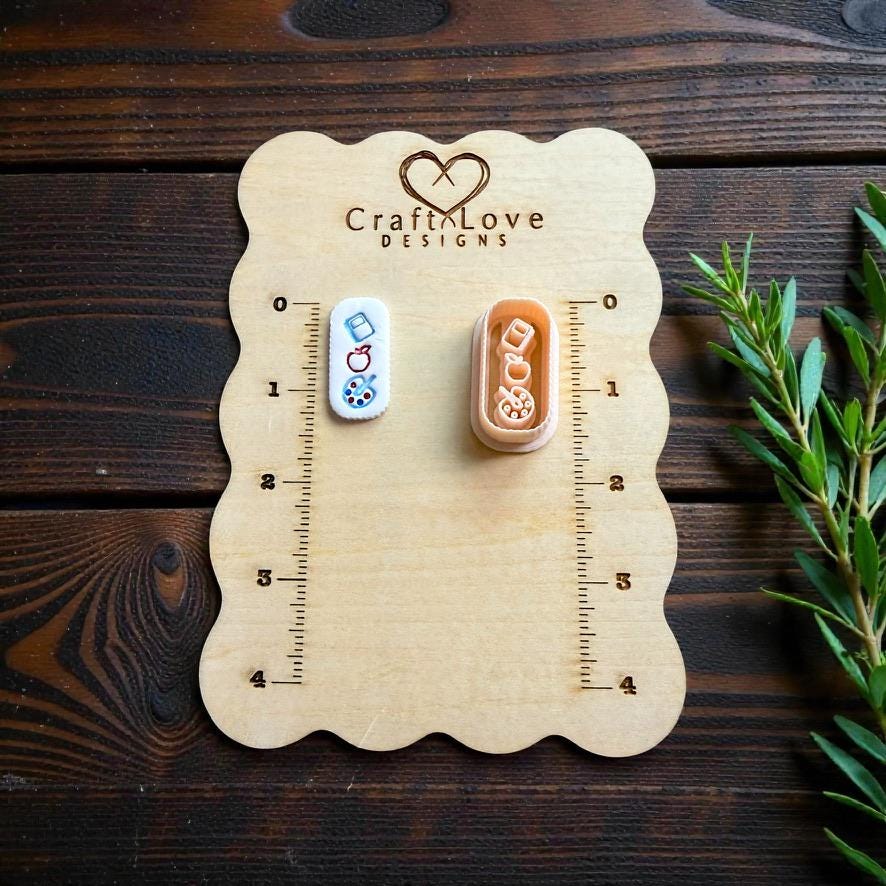 Teacher earrings clay cutter displayed on CraftLove Designs wooden measurement board with rustic wood background and greenery