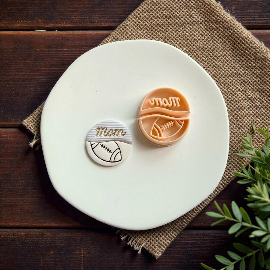 Finished football mom polymer clay earring and cutter displayed on white ceramic plate with rustic wood background