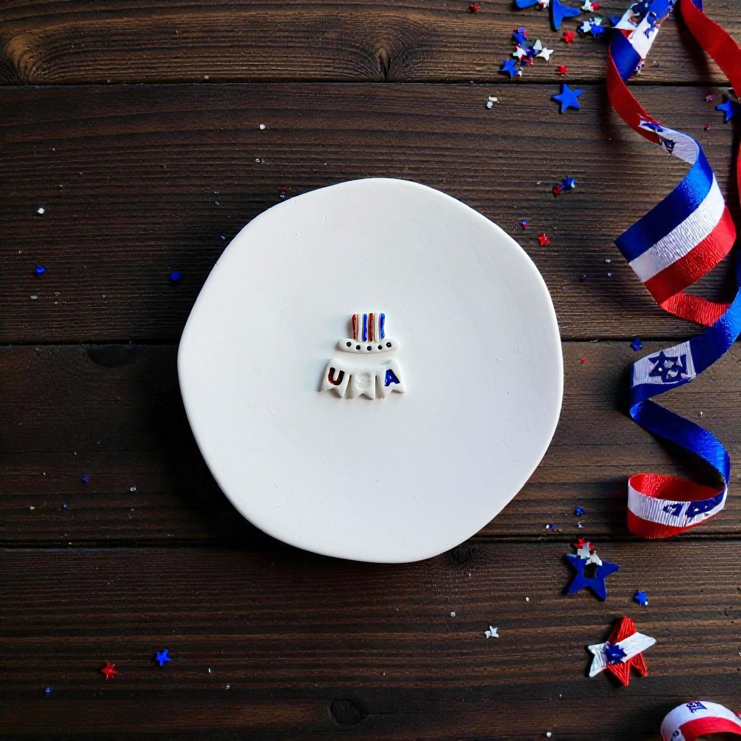 Finished Fourth of July clay earring design featuring an Uncle Sam hat and USA banner on a white round surface