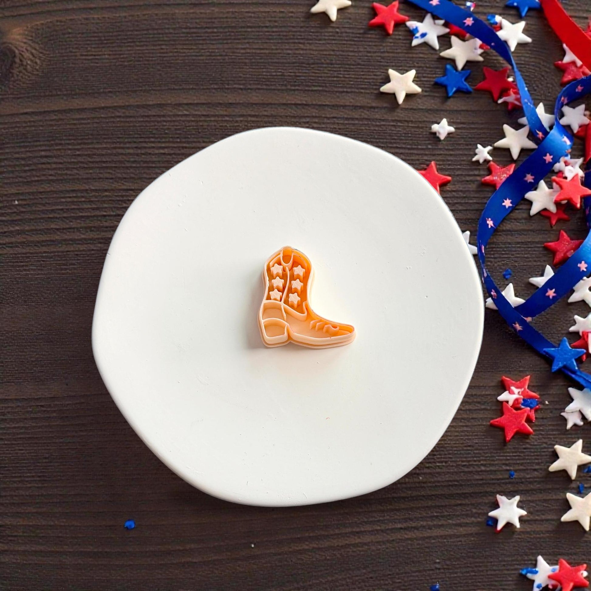 Close up of western cowboy boot polymer clay cutter on white display surface with Fourth of July star decorations and ribbon