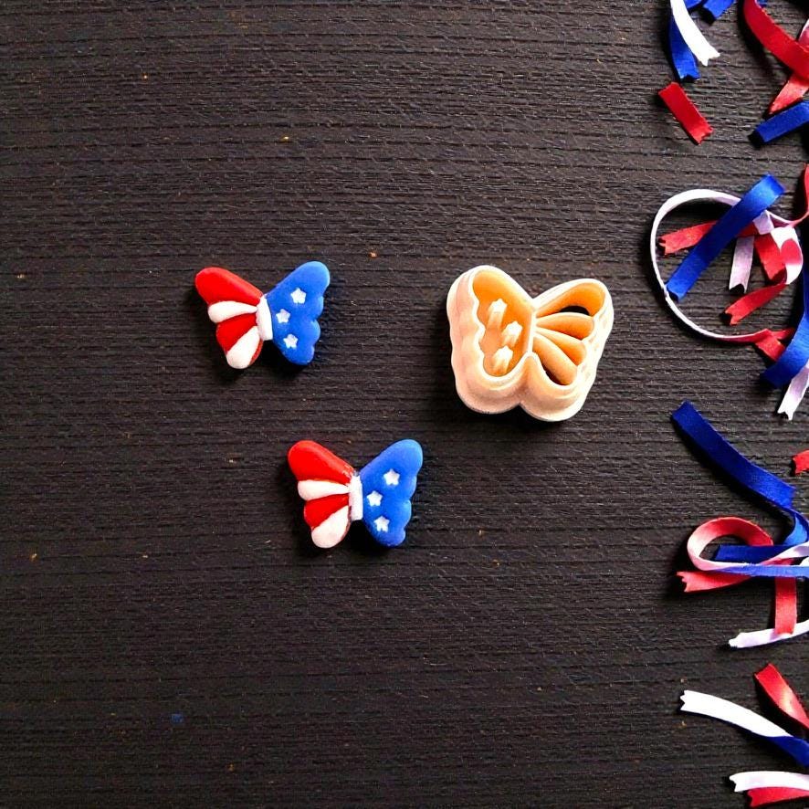 Close up of patriotic butterfly clay earrings beside matching butterfly cutter on dark wooden background