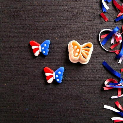 Close up of patriotic butterfly clay earrings beside matching butterfly cutter on dark wooden background