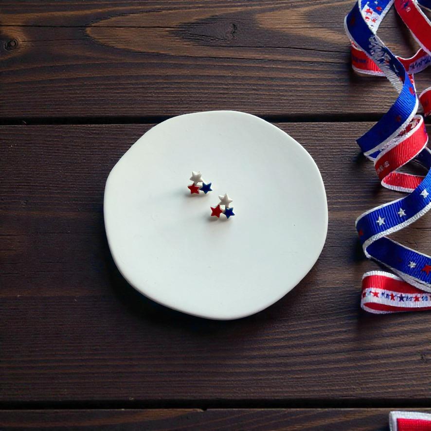 Small patriotic triple star polymer clay earrings on white display surface with red white and blue ribbon