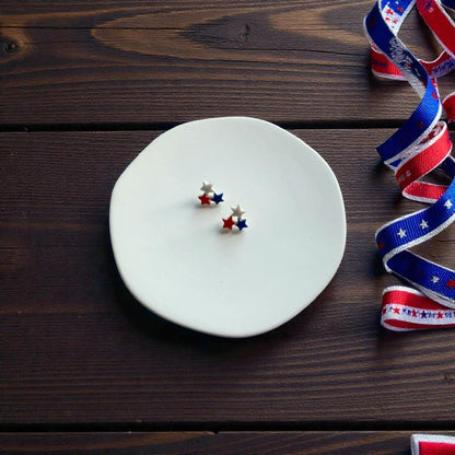 Small patriotic triple star polymer clay earrings on white display surface with red white and blue ribbon
