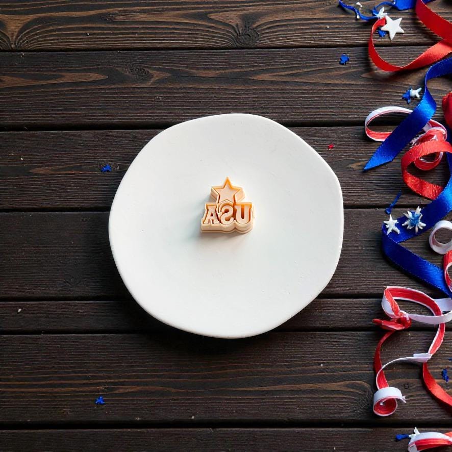 USA letter polymer clay cutter displayed on white clay surface with patriotic ribbon and confetti