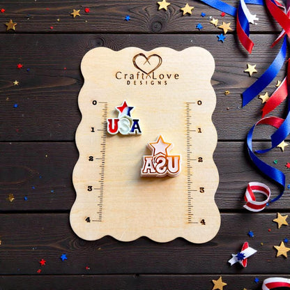 Patriotic USA polymer clay stud earrings displayed on wooden jewelry board with festive red white and blue decorations