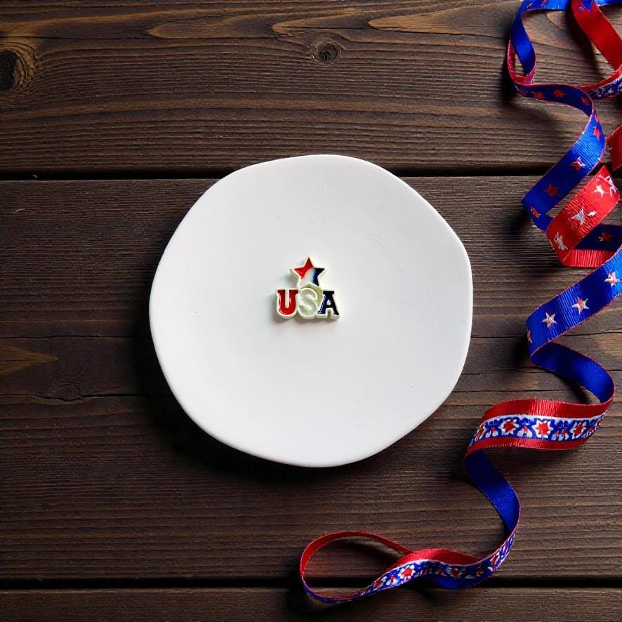 Small USA star earrings displayed on white round clay slab with Fourth of July ribbon decorations