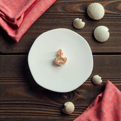 Nautical seashell anchor polymer clay cutter displayed on white clay slab with coastal shell decorations and pink fabric