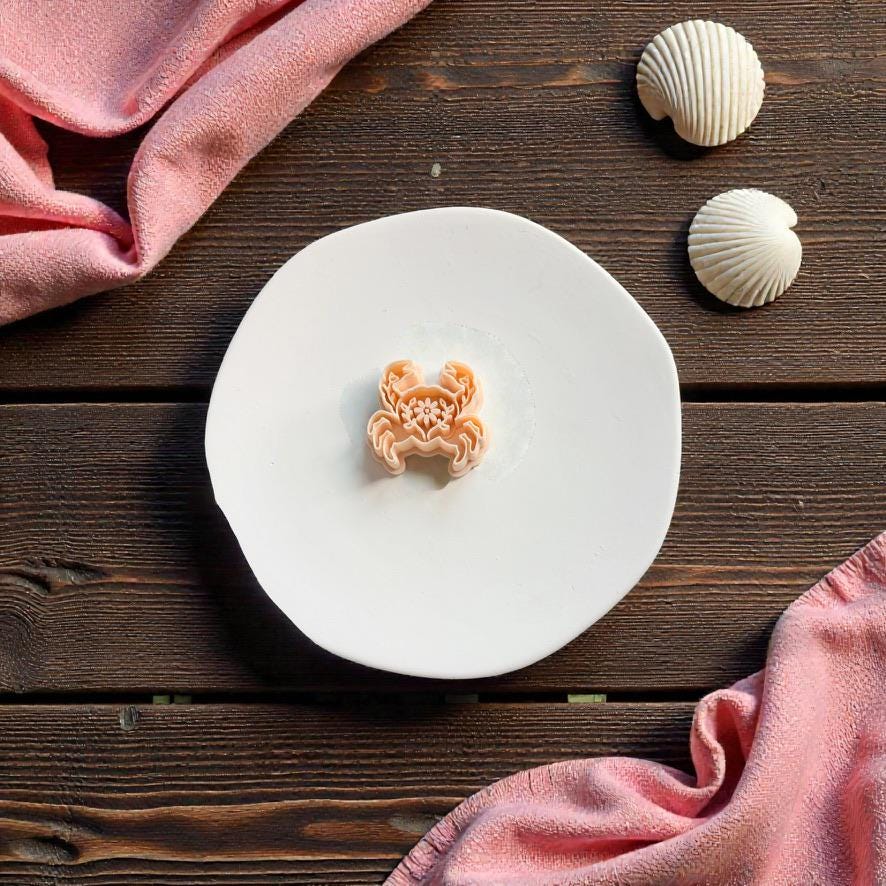 Folk art crab polymer clay cutter displayed on white ceramic plate with seashell decorations and beach themed styling