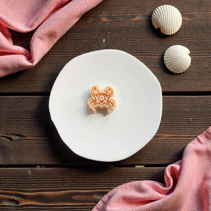 Folk art crab polymer clay cutter displayed on white ceramic plate with seashell decorations and beach themed styling