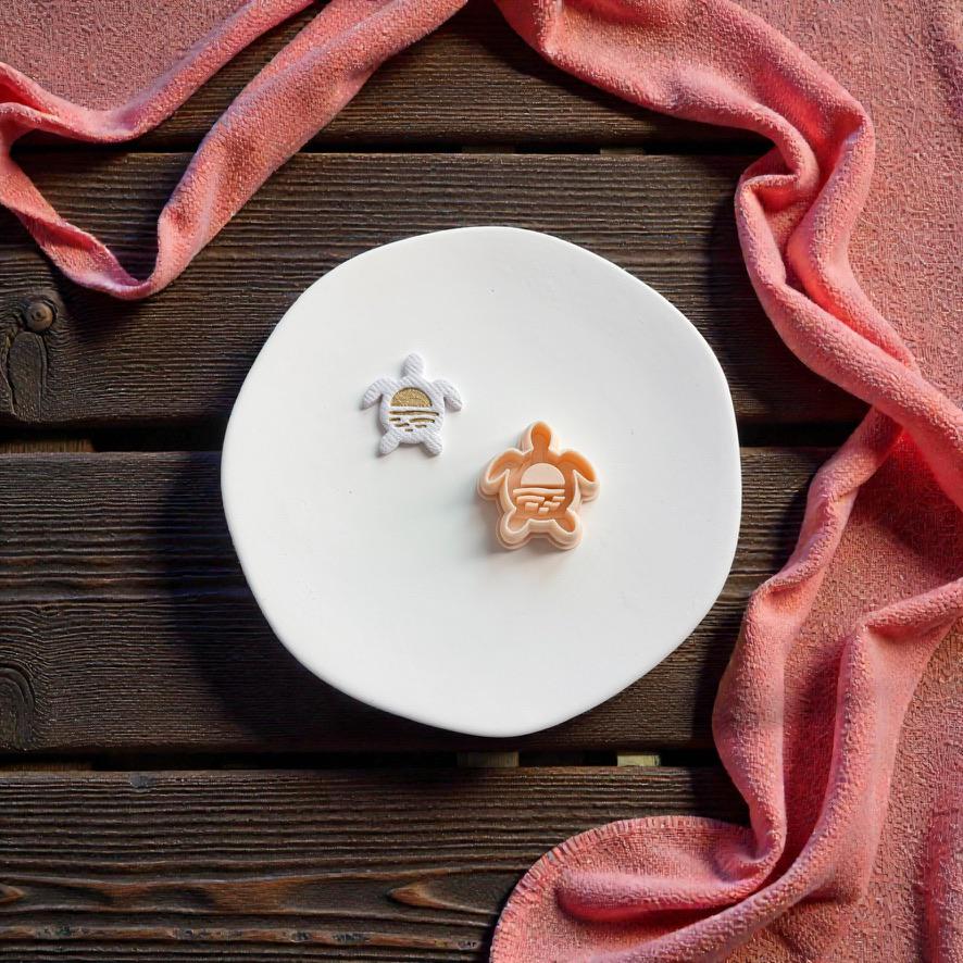 Sunset center turtle polymer clay cutter displayed beside matching finished turtle clay piece on white ceramic plate