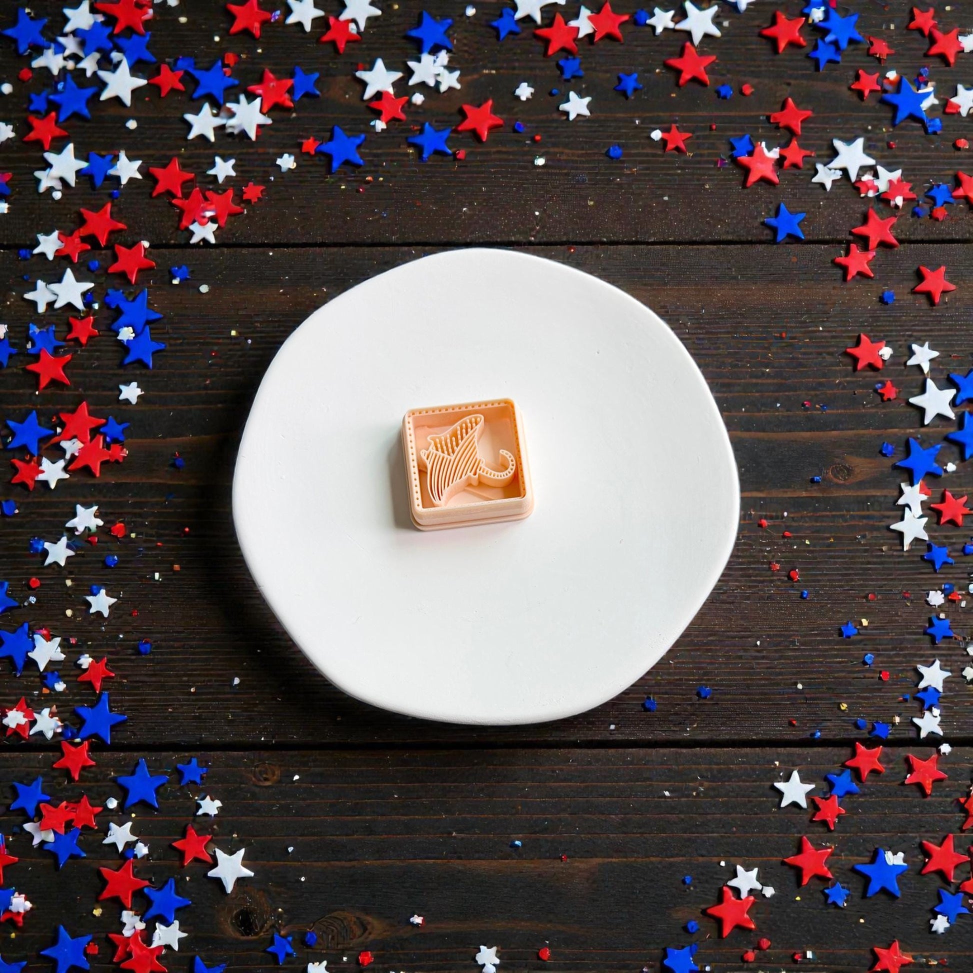Patriotic stingray polymer clay cutter displayed on white ceramic plate surrounded by red white and blue star confetti
