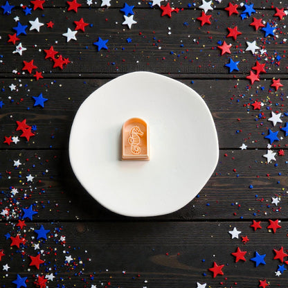 Patriotic seahorse clay cutter displayed on white ceramic plate with festive Fourth of July star confetti background