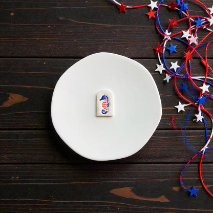 Finished patriotic seahorse clay piece with red white and blue Americana design displayed on white ceramic plate with patriotic ribbon decorations