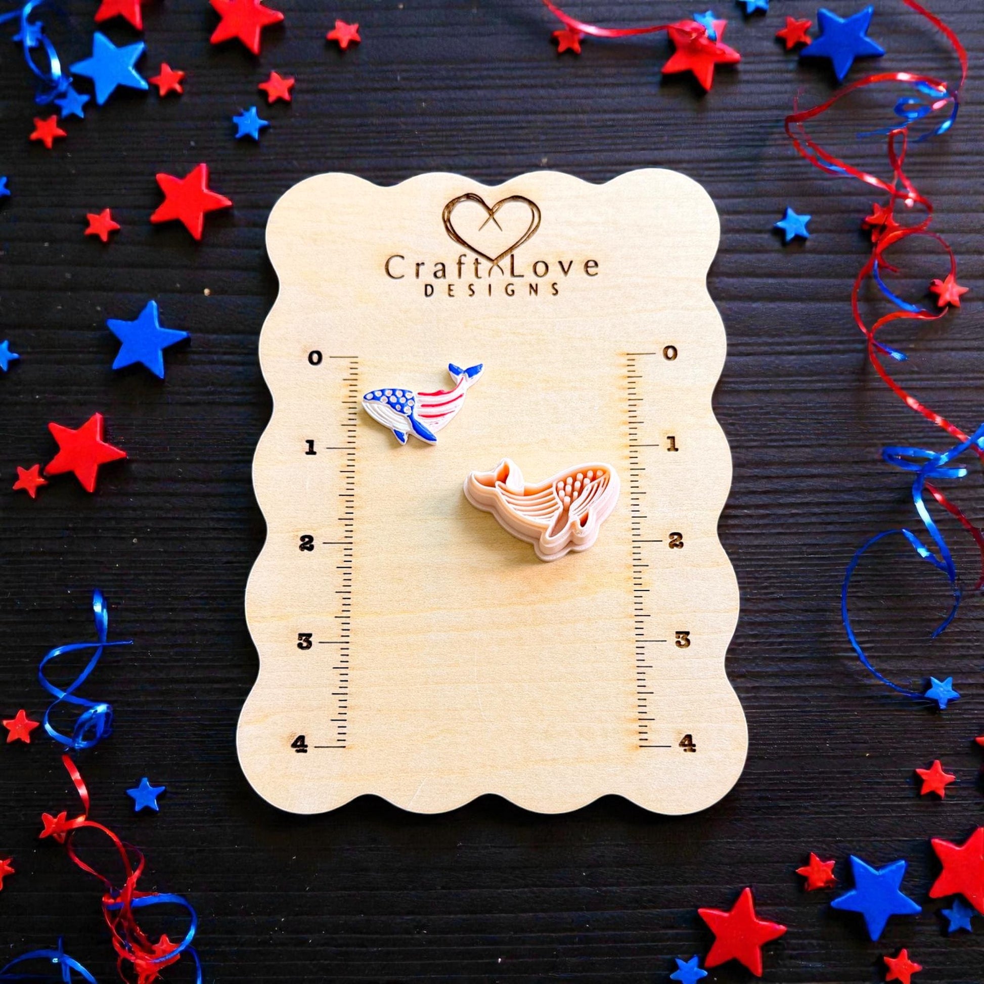 Patriotic whale polymer clay cutter and finished clay design displayed on CraftLove Designs wooden measurement board with patriotic ribbons and stars