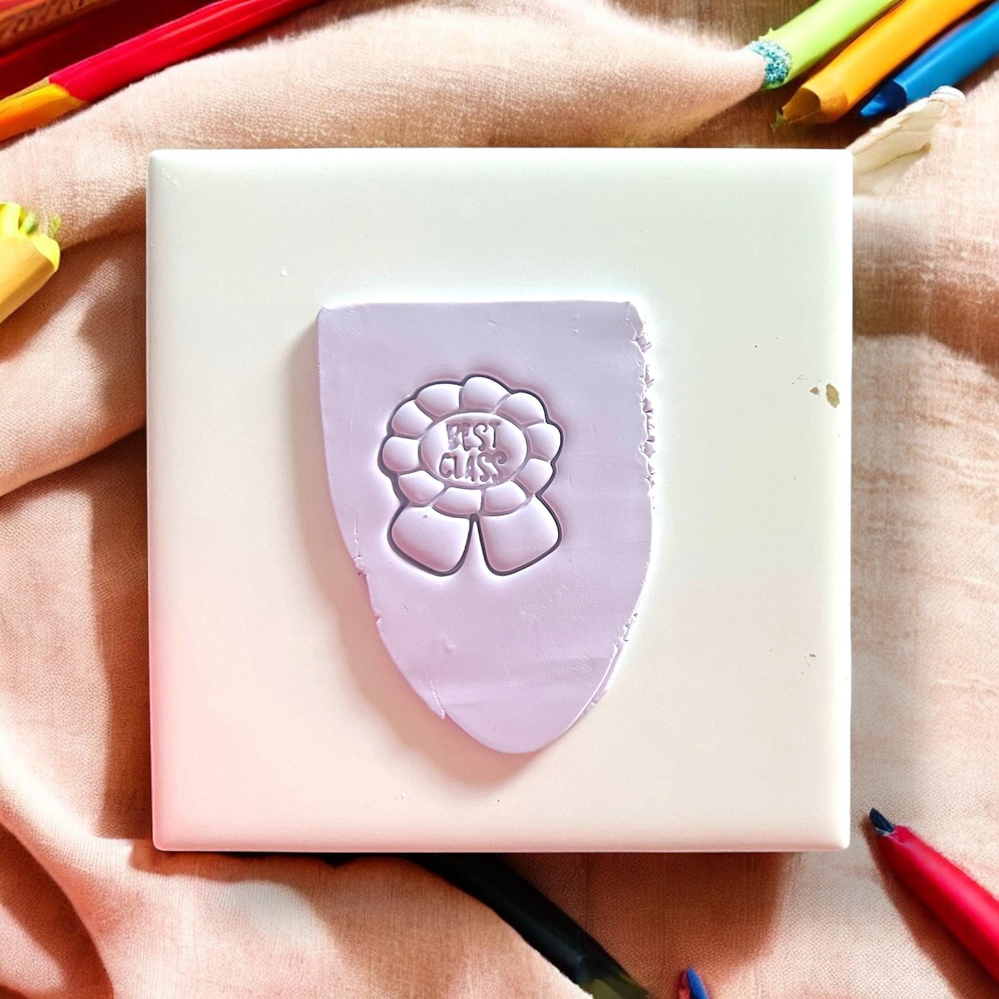 Purple flower-shaped stamp on a white block with colorful pencils in the background