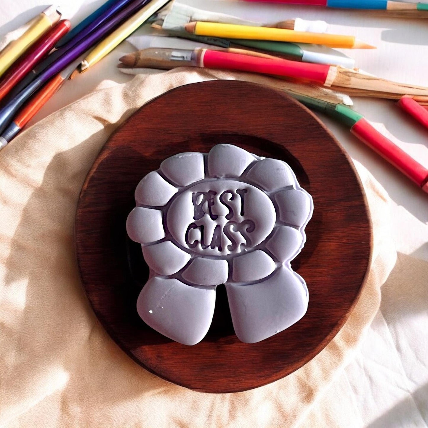 Gray clay mold with 'Moshi Moshi' text on a wooden board, surrounded by art supplies.