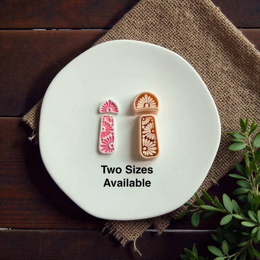 Two sizes of boho daisy polymer clay cutter set displayed side by side on white ceramic plate with rustic fabric background