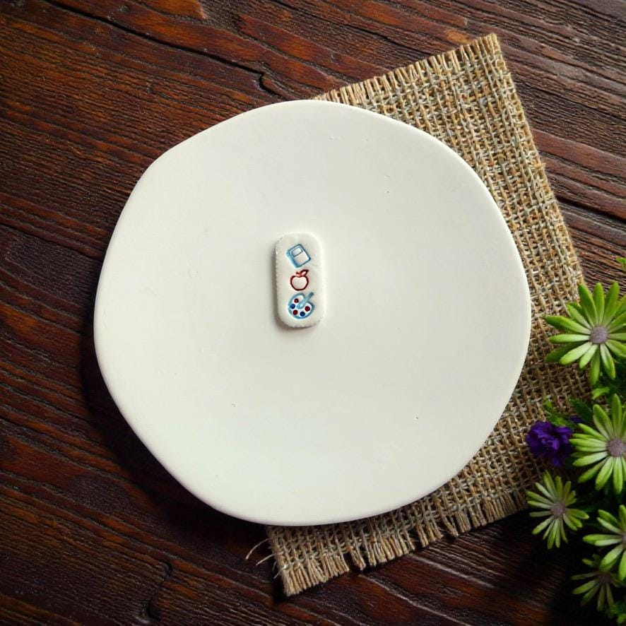 Finished teacher themed clay earring featuring book apple and paint palette icons on white ceramic plate