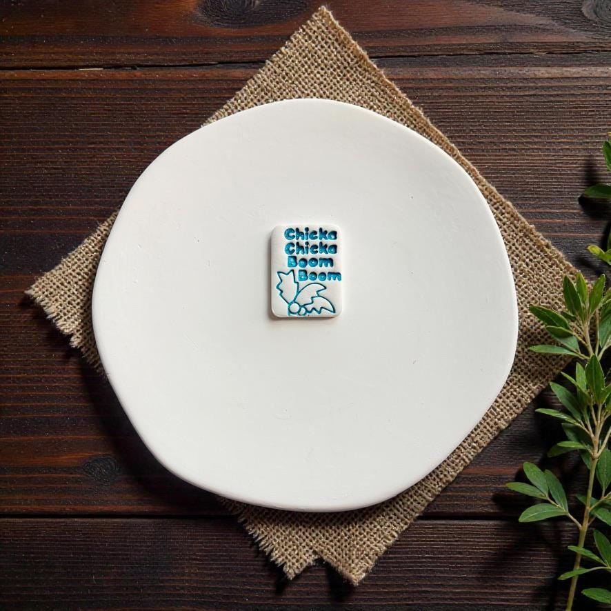Finished nostalgic alphabet themed clay earring on white ceramic plate with rustic burlap background