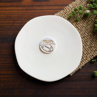 Finished football mom polymer clay earring displayed on white ceramic plate with rustic wood background